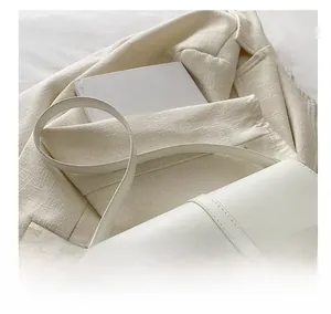 Détail d'un sac besace blanc avec boucle dorée sur un fond en tissu de tweed