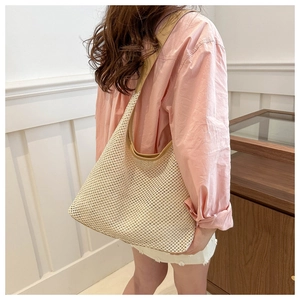 Detail of hand-woven straw shoulder bag with contrast brown trim on a fashion model