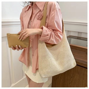 Détail du sac hobo en paille tressée et de la pochette en cuir portés par un mannequin