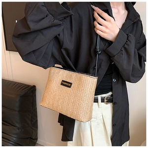 Close-up of woven straw bucket bag featuring a black leather patch and slim shoulder strap