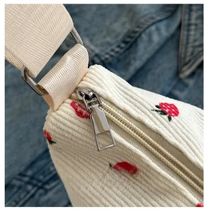 Detail of strawberry embroidery on white corduroy bag with smooth silver metal zipper