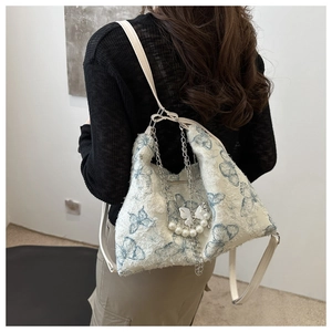 Close-up of plush white shoulder bag with blue butterfly print, pearl chain and charm