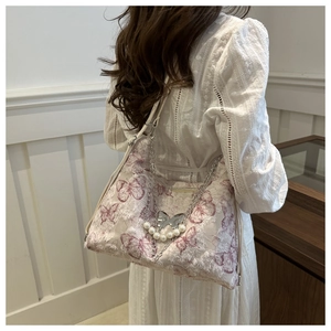 Detail of floral butterfly tote with silver chains and pearl charms on beige fabric