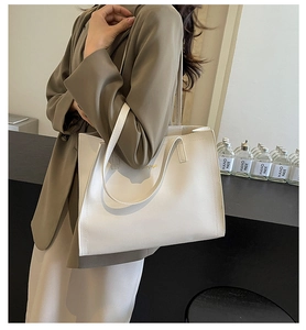 Close-up of white leather tote bag with gold logo shown on model's shoulder for size