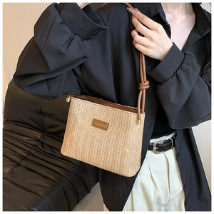 Close-up of woven straw bucket bag with brown leather patch and thin shoulder strap