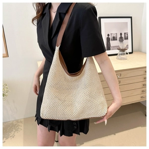 Detail of hobo straw shoulder bag with brown leather strap worn by a model in interior