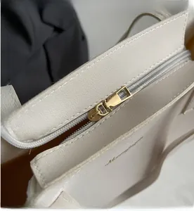 Close-up of the smooth golden metal zipper and fine-textured cream leather tote bag