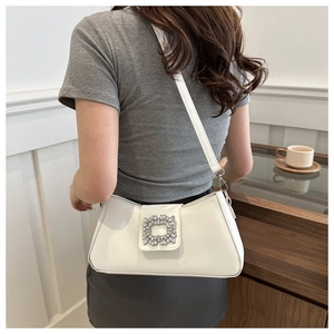 Chic white baguette bag with rhinestone square buckle worn on shoulder in a cafe