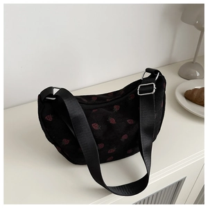 Detail of black corduroy dumpling bag featuring red strawberry embroidery and strap
