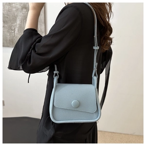 Close-up of light blue pebble grain saddle bag worn by model over a black dress