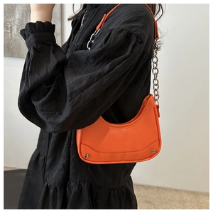 Detail of bright orange crescent bag with silver rivet studs and chain shoulder strap