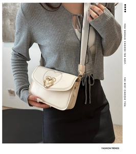 Chic beige crossbody bag with gold heart buckle and wide strap shown on a model