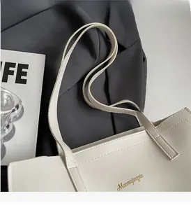 Detail of off-white PU leather tote bag with gold brand logo and slim handle straps