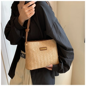 Detailed view of woven straw bucket bag with brown leather FASHION patch and knotted strap
