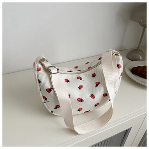Detail of white corduroy crescent bag with red strawberry print and adjustable strap