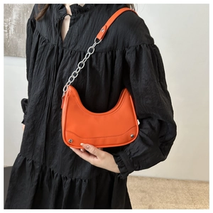 Detail view of bright orange crescent underarm bag with silver chain and metal rivets
