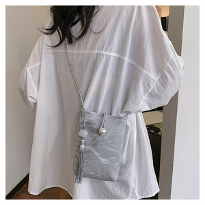 Macro-opname grijze mini crossbody tas met parelsluiting en een lange kwastjes hanger