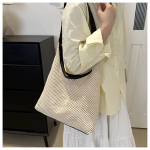 Detail of beige woven tote bag with black contrast straps on model in summer outfit