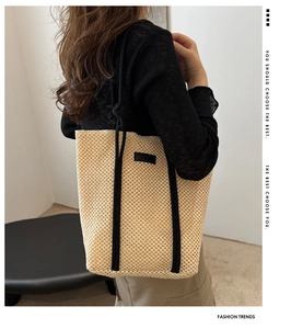 Detailed side view of a large woven straw tote bag with black strap accents on model