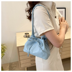 Close-up of light blue bucket bag with bow detail worn by a model in a cozy room