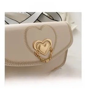 Close-up of heart-stitched cream saddle bag with gold heart clasp and metal chain detail