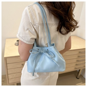 Dettaglio di una borsa a secchiello celeste con fiocco indossata da una modella a casa