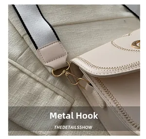 Close-up of golden hardware hook and striped wide strap on beige crossbody bag