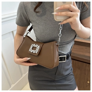 Detail showing brown leather texture and large square crystal buckle on the shoulder bag