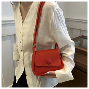 Detail of red lychee textured saddle bag with circular buckle on white shirt