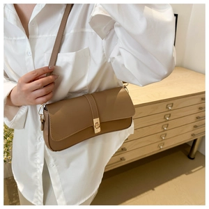 Détail d'un sac à bandoulière en cuir marron avec fermoir doré porté par un mannequin