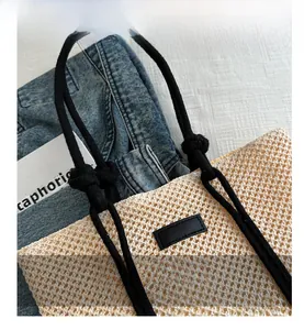 Close-up of woven straw tote bag with black rope handles and a minimal leather patch