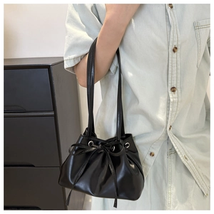 Detail of black glossy drawstring bucket bag with leather bow and silver metal eyelets