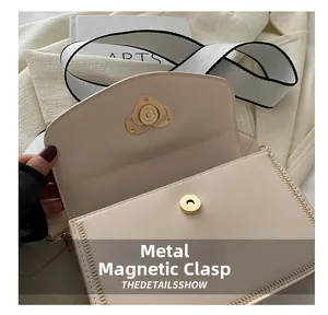 Detail of golden heart-shaped magnetic clasp and stitch on beige crossbody bag