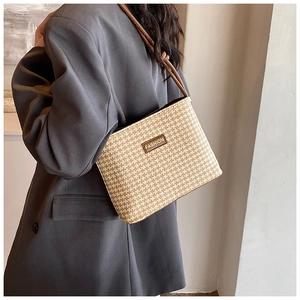 Detail of a beige woven straw bucket bag with a brown leather patch and shoulder strap