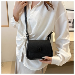 Detail of black lychee grain leather saddle bag on white shirt model outfit