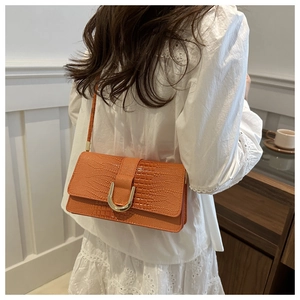 Sac bandoulière orange avec texture crocodile et boucle en U dorée sur un mannequin