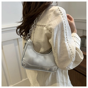 Silver metallic crescent bag with chunky chain strap worn over the shoulder by a model
