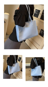 Detail view of light blue tote bag with white contrast stitching and gold logo lettering