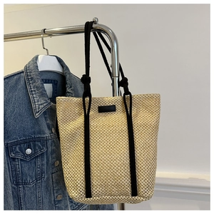 Detail of hand-woven straw tote bag with black rope handles and leather patch on cream base