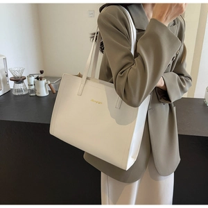 Minimalist beige PU leather tote bag with long handles shown on a model in a warm setting