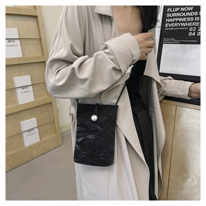 Close-up of black crossbody bag featuring textured fabric and a large pearl decoration