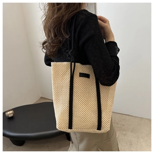 Detail of beige hollow woven tote bag featuring contrasting black canvas straps and texture