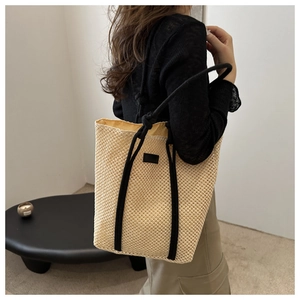 Close-up of a woven straw tote bag featuring black rope handles and minimalist leather patch