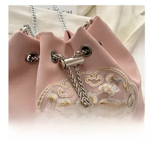 Detail of pink satin bucket bag with floral embroidery and silver chain strap