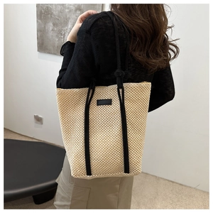 Detail of hollow-out woven straw tote with black rope handles and leather patch