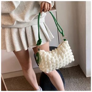 Detailed shot of white bubble textured bag with green knotted handle and flower charm