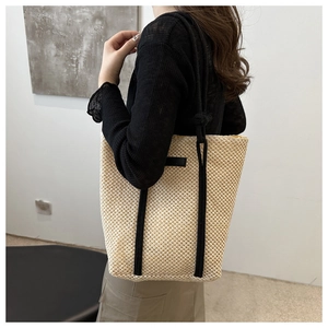 Close-up of beige woven tote bag featuring black rope handles and vertical strap detail
