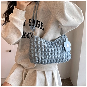 Detail of light blue bubble textured shoulder bag with floral charm worn by a model