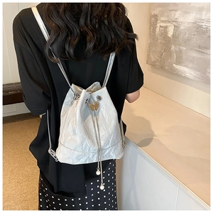 Detail of silver pleated backpack featuring a golden butterfly clasp and pearl drawstrings