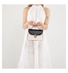 Detail of elegant color-block handbag with gold rotary lock and top handle shown on model